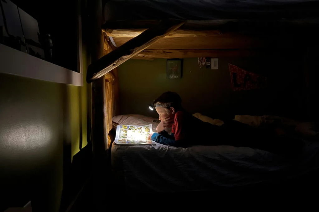 Child reading a book at night under a bunk bed with a headlamp, showing how supporting emotional regulation in children can start with calming bedtime routines in a nurturing home.