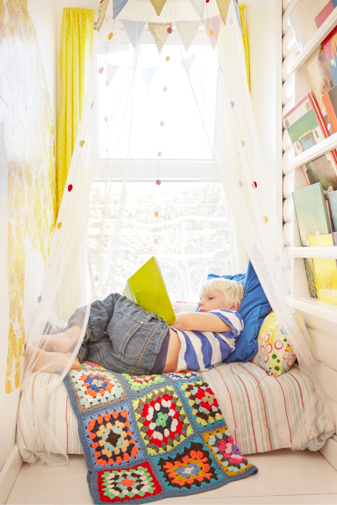 Child reading a book in a bright, cozy reading nook with pillows and a colorful blanket, showing how parenting neurodiverse kids can include creating nurturing, calm spaces at home.