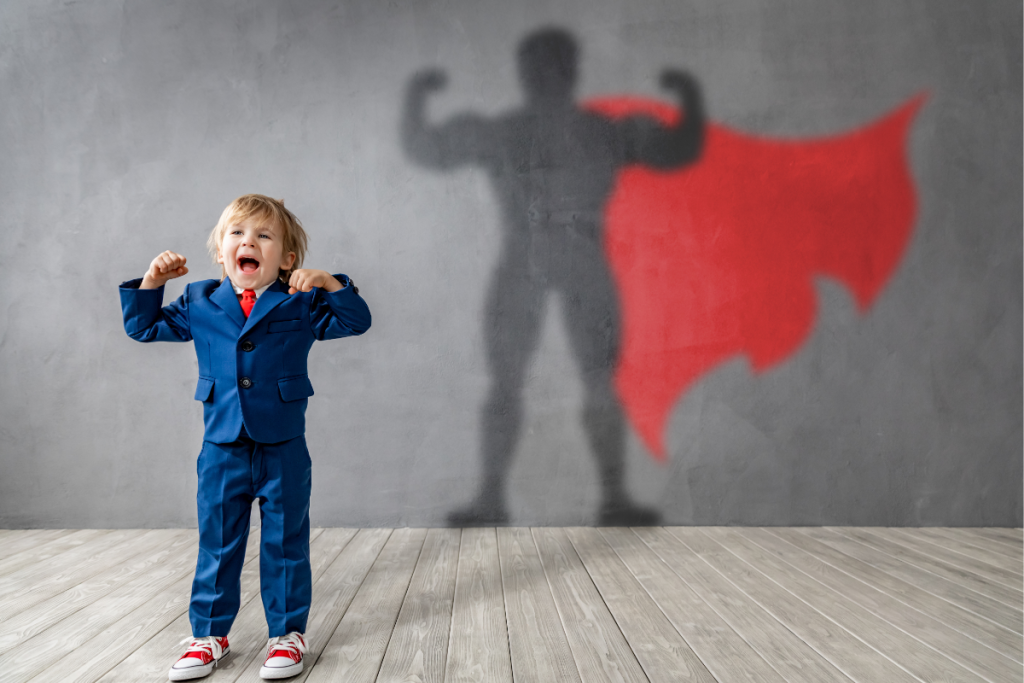 Young boy in a blue suit flexing his arms with a superhero shadow behind him, symbolizing confidence and hidden strength in neurodivergent children
