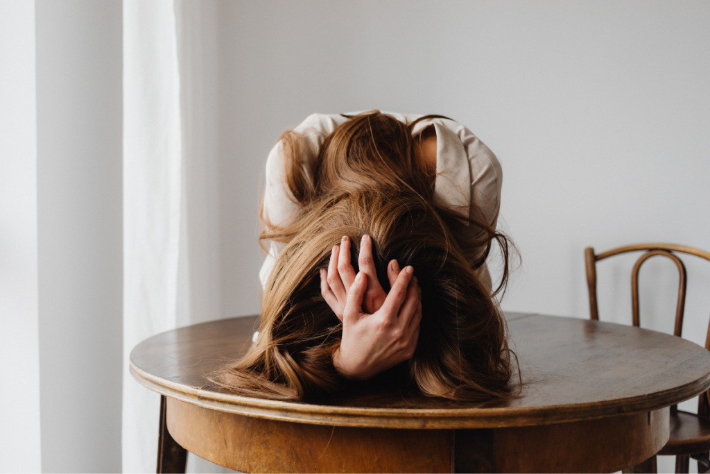 Exhausted mother with head in hands at a table, showing the emotional toll of ND parent burnout.