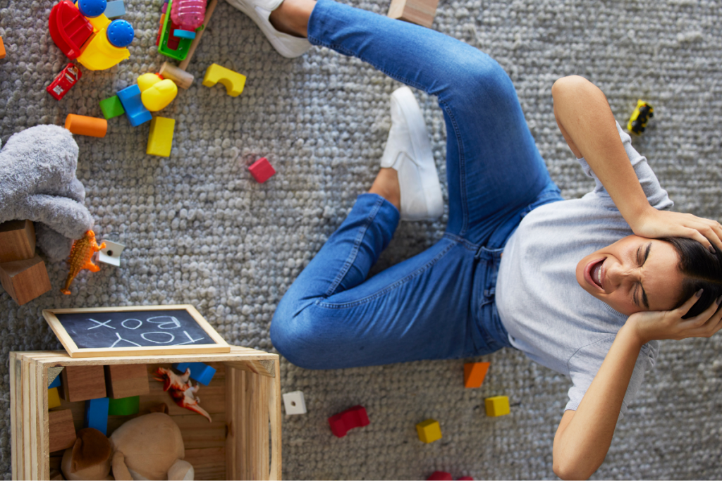 Stressed mom lying on the floor surrounded by toys, showing the reality of ND parent burnout and the need for self-care.