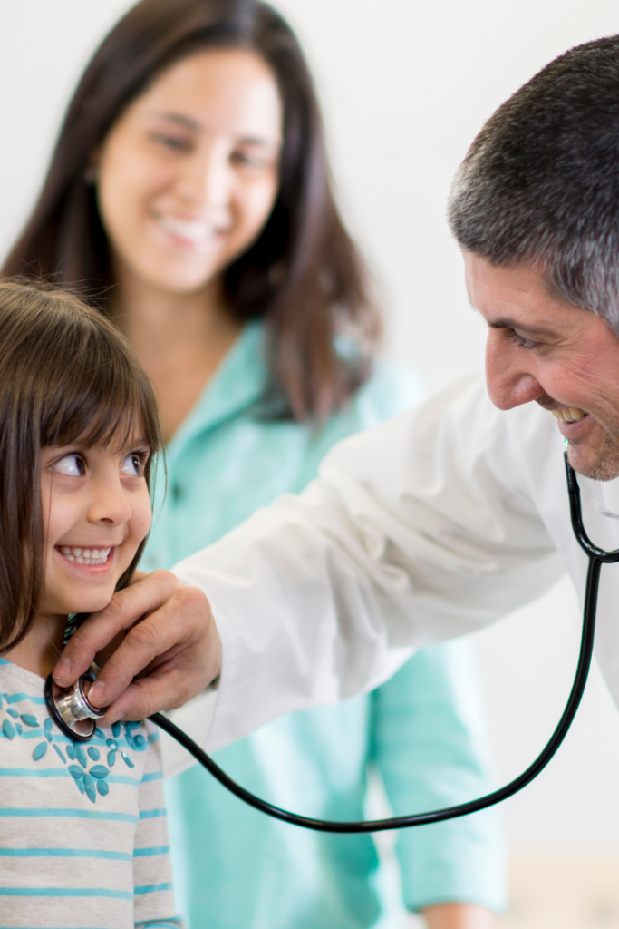 Mother smiling as a doctor listens to her daughter’s heartbeat, showing what it means to be an advocate for your child in healthcare and education.