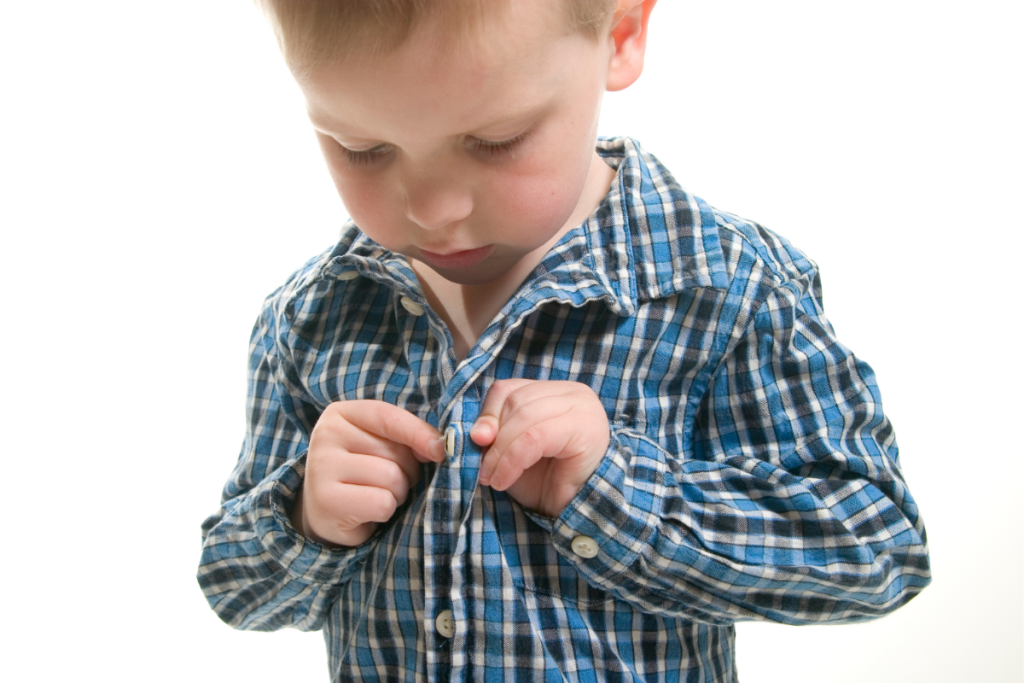 Young boy buttoning his shirt, a milestone moment in empowering independence in ND children.