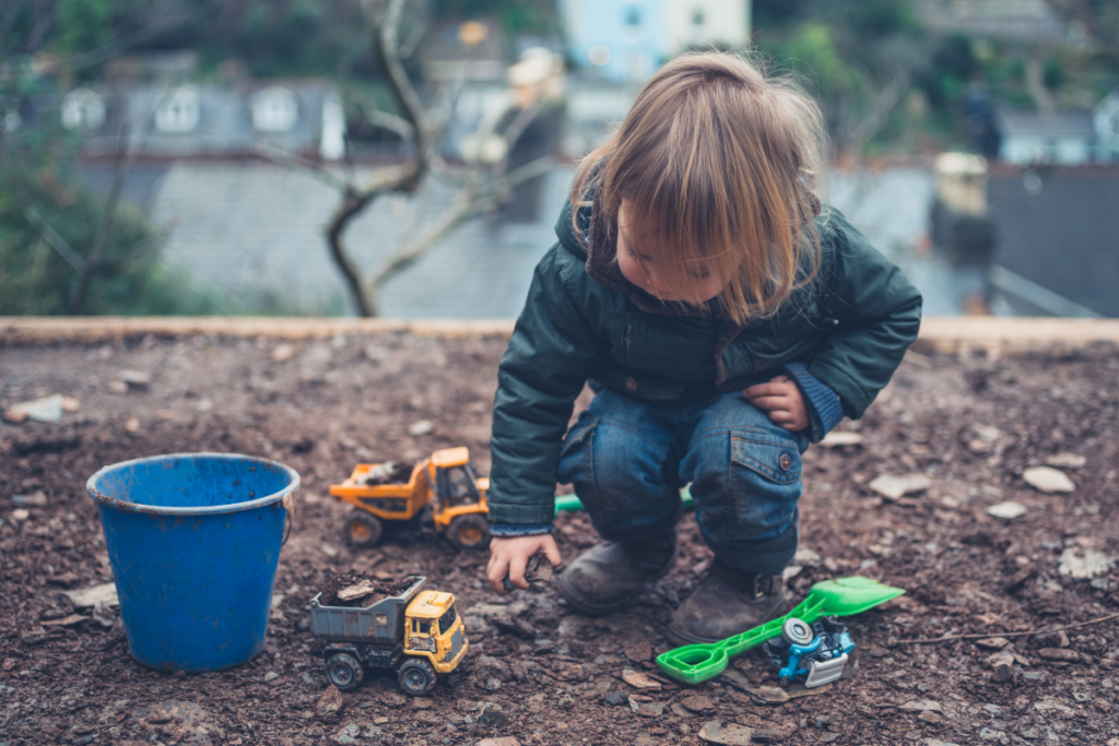 Young ND child playing with toy trucks and dirt outside, showing how nurturing childhood passions helps them thrive with creativity and focus.