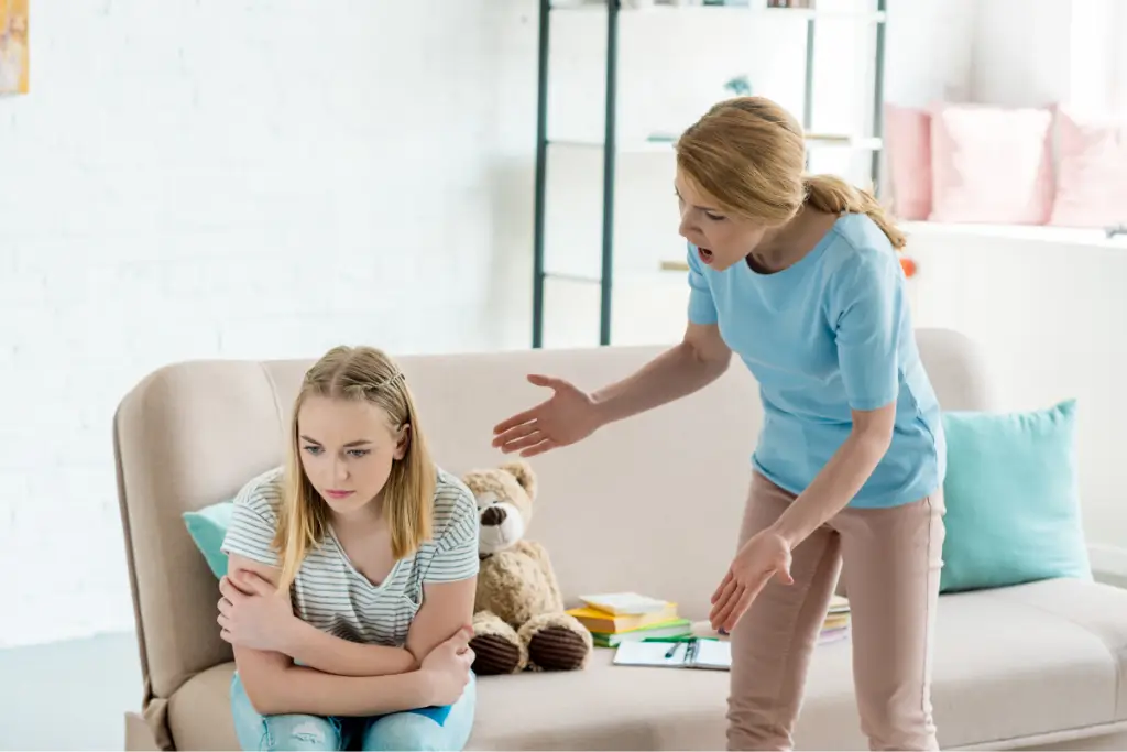A mother yells while her teenage daughter sits on the couch looking upset, showing the tension that happens when parents react vs respond instead of pausing and staying calm during conflict.