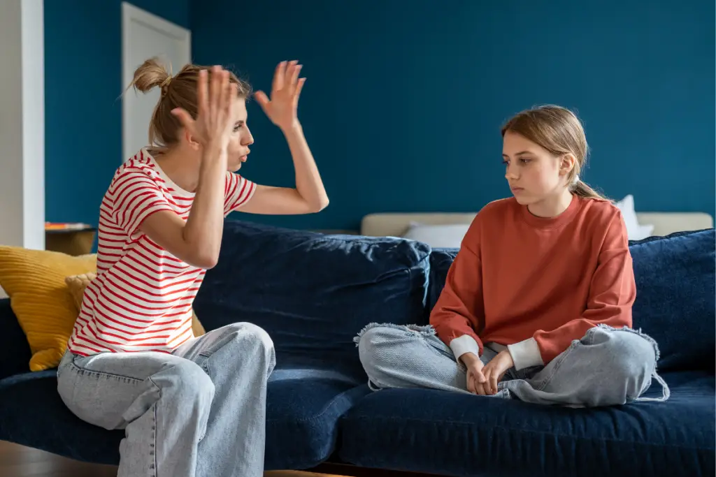 A frustrated parent raises her hands while a withdrawn teen sits quietly on the couch, illustrating the react vs respond struggle many ND mamas face during emotional moments.