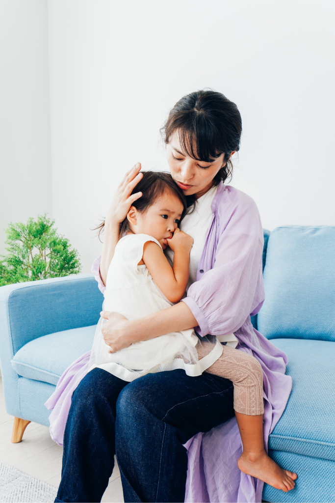 A mother gently comforting her distressed child on the couch, modeling the react vs respond approach by choosing calm connection over emotional escalation.