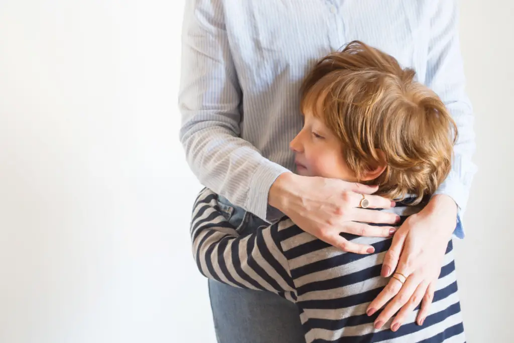 A young boy hugs his mother tightly, symbolizing calm connection and emotional safety — the heart of choosing to react vs respond in mindful, compassionate parenting.