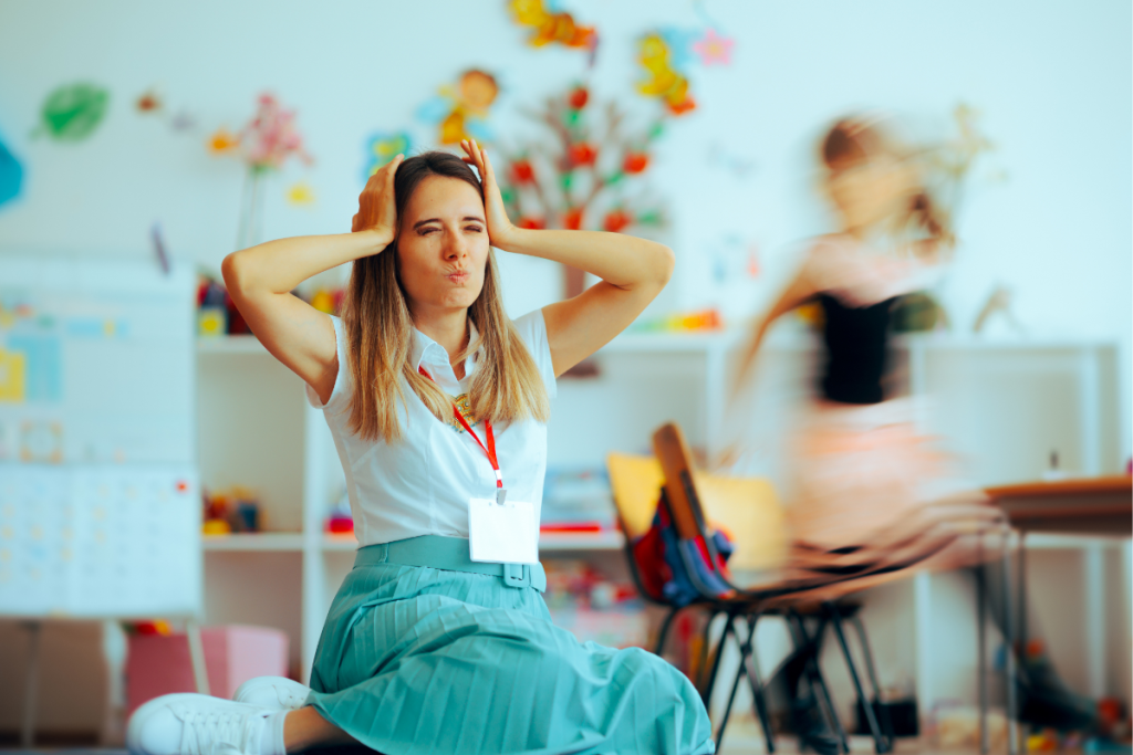 A stressed woman sits on the floor of a classroom holding her head while a child rushes past, illustrating why advocacy isn’t optional for overwhelmed mamas.