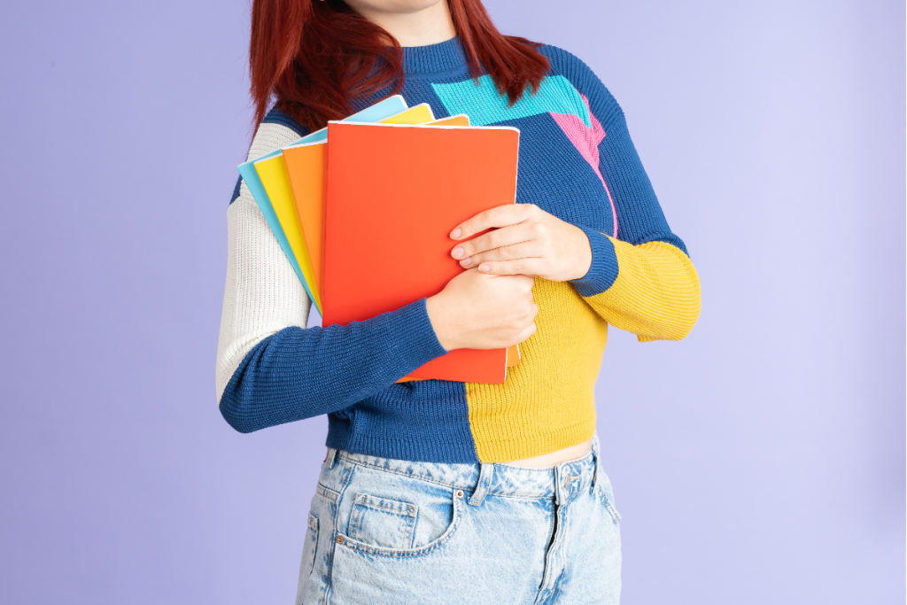 A mama holds a stack of colorful folders and notebooks, symbolizing IEP meeting prep for ND mamas organizing materials before a school meeting.