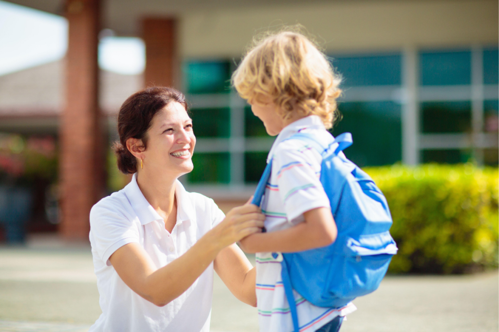 A mama helps her child adjust a backpack outside a school building, reflecting IEP meeting prep for ND mamas focused on supporting their child’s daily school experience.