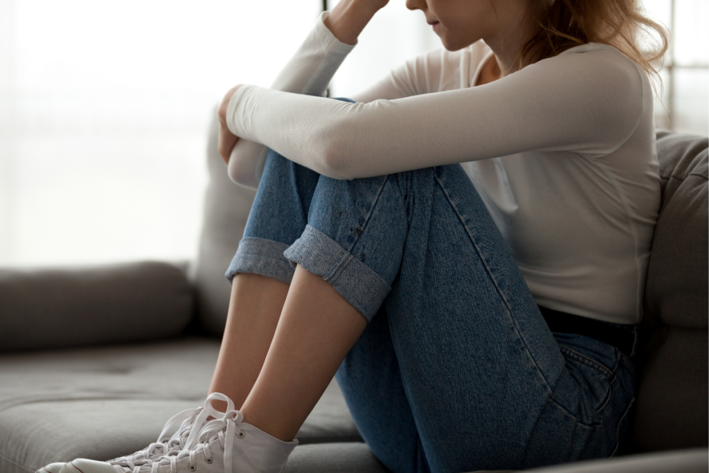 A neurodivergent teen or young adult sitting curled up on a couch, reflecting the emotional impact of neurodivergent lies and internalized self-doubt.