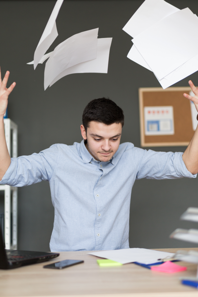 A person at a desk throwing papers into the air, illustrating the overwhelm and pressure created by neurodivergent lies about productivity and performance.