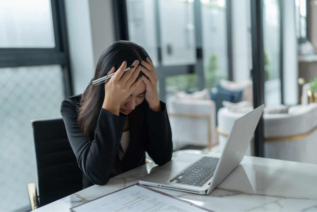 A woman holding her head at work, illustrating how neurodivergent lies about performance and worth can lead to chronic overwhelm.