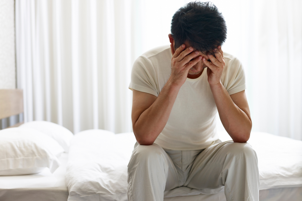 A man sitting on a bed with his head in his hands, reflecting emotional overwhelm caused by neurodivergent lies about strength, self-control, and resilience.