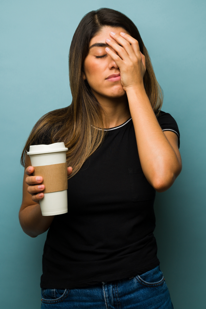 A mother holding a coffee cup with her hand covering her face, illustrating maternal guilt and emotional exhaustion after a late or missed diagnosis.