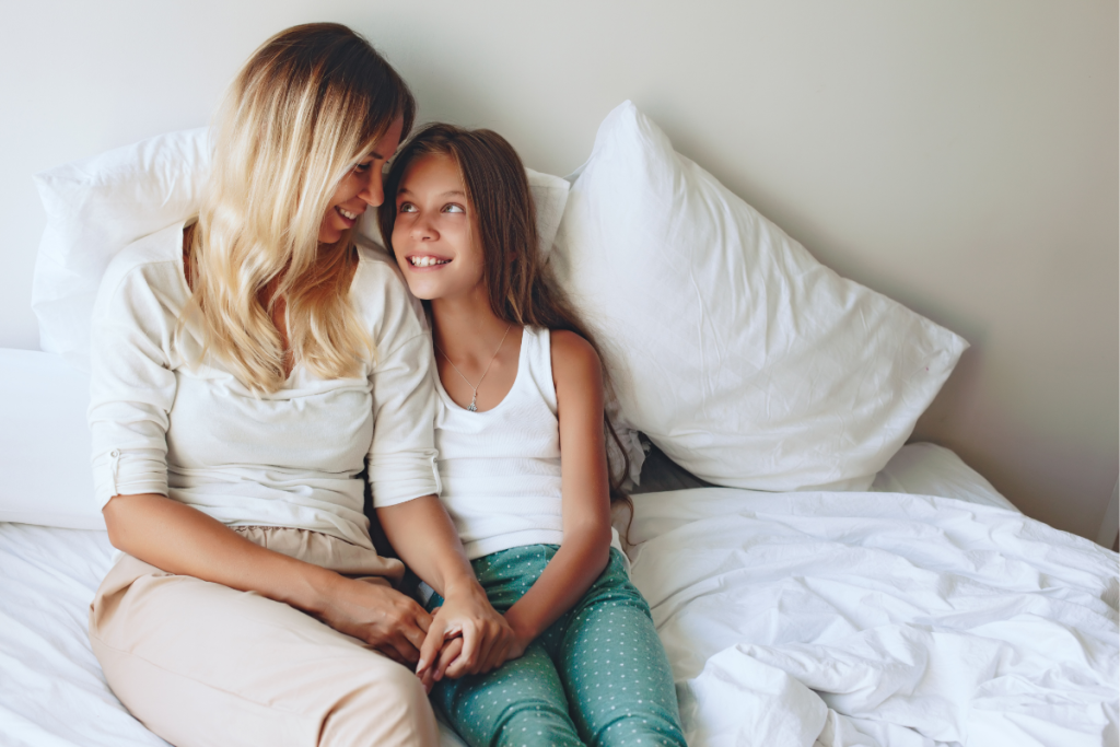 A mother and daughter sitting together on a bed, sharing a quiet moment that reflects maternal guilt, connection, and reassurance after a late or missed diagnosis.
