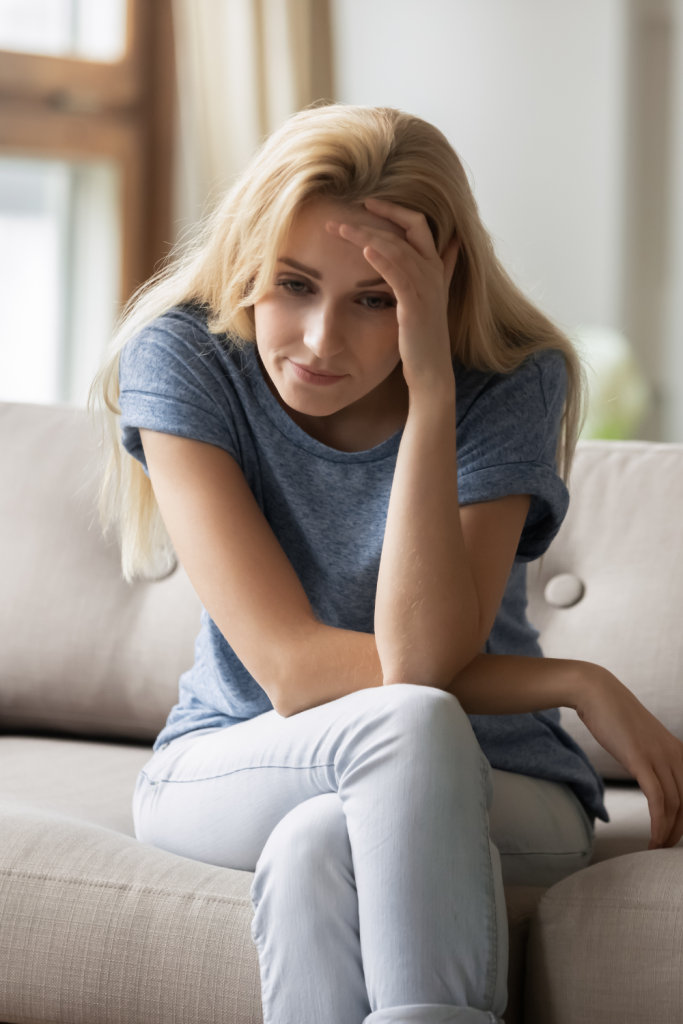 A mother sitting on a couch with her hand on her forehead, reflecting the emotional toll families feel when schools don’t see the problem and a child continues to struggle.