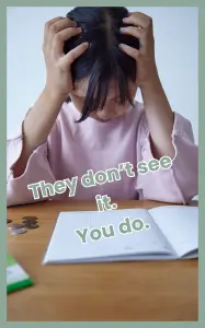 A school-aged child holding their head in frustration while sitting at a desk with an open workbook, illustrating the stress families face when schools don’t see the problem despite a child struggling.