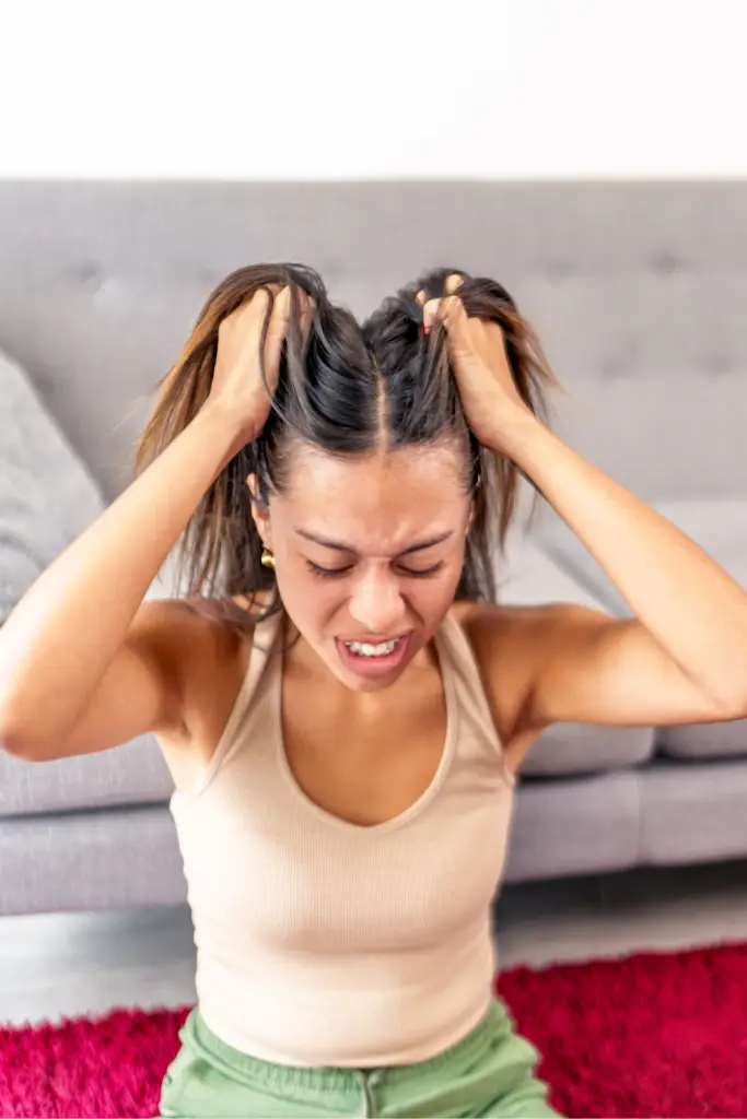 Young woman sitting on the floor pulling her hair in frustration, representing emotional dysregulation and adult ADHD impulse control at home.